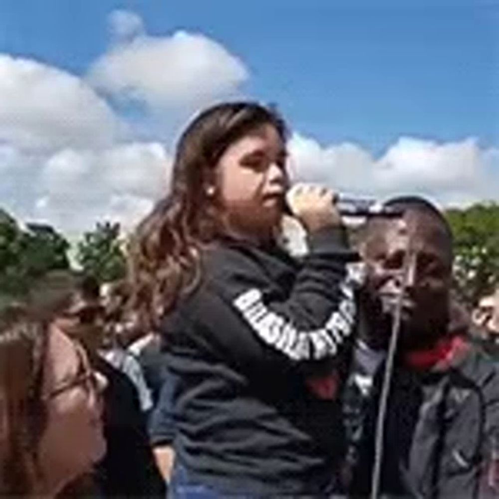 a young girl is singing into a microphone in front of a crowd .