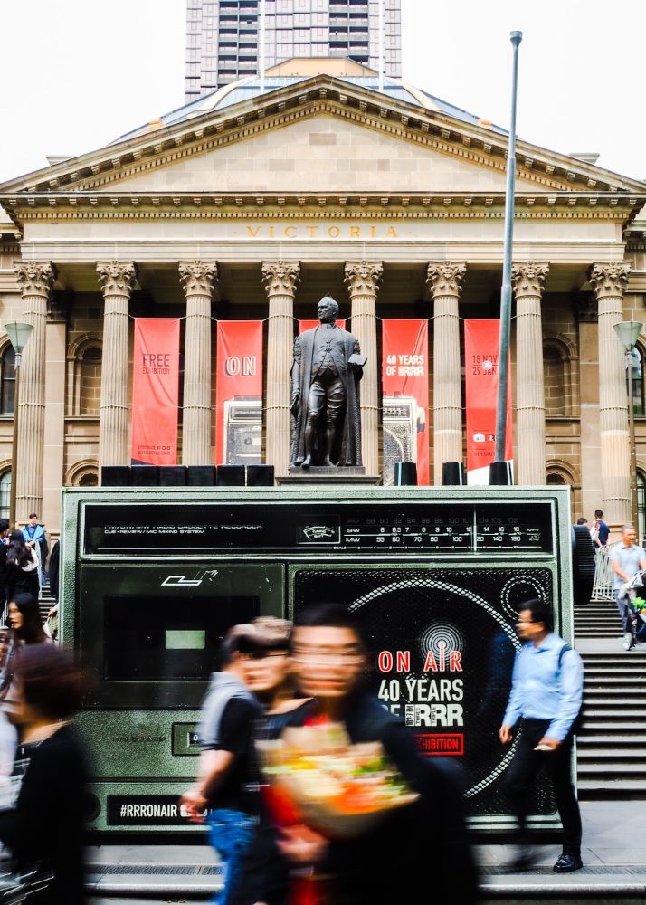 A giant old school style radio stands in front of Victoria's State Library as pedestrians walk past.