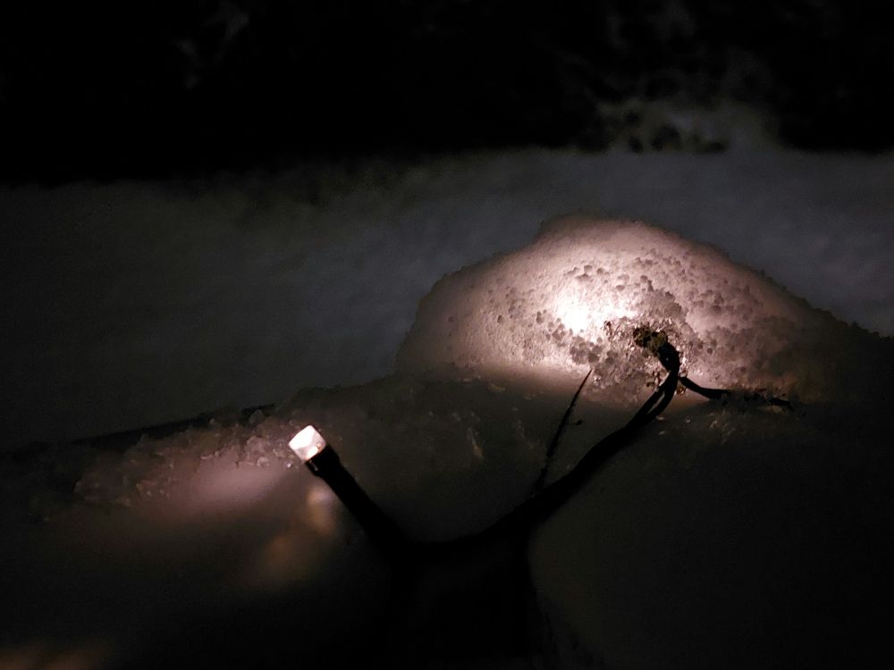 Schnee auf dem Balkongeländer, der eine Lichterkette bedeckt. Dadurch leuchtet der Schnee.