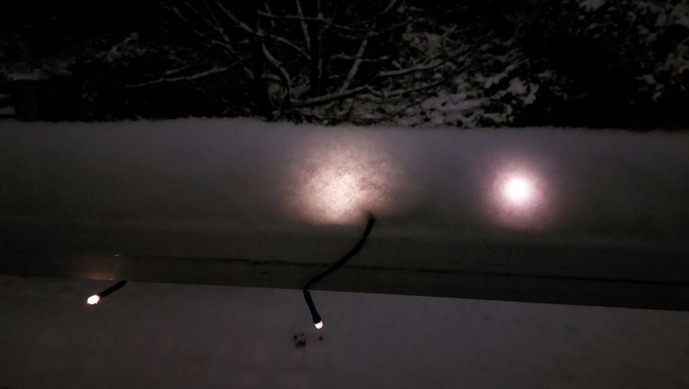 Schnee auf dem Balkongeländer, der eine Lichterkette bedeckt. Dadurch leuchtet der Schnee.