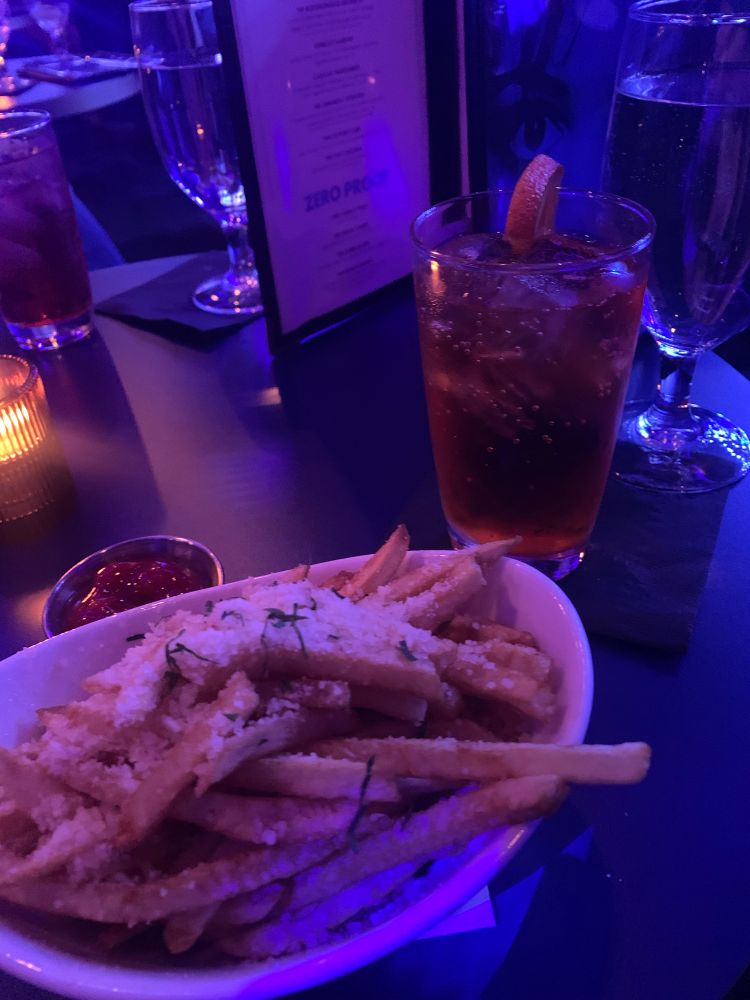 A mocktail in a tall glass and a plate of Parmesan truffle fries