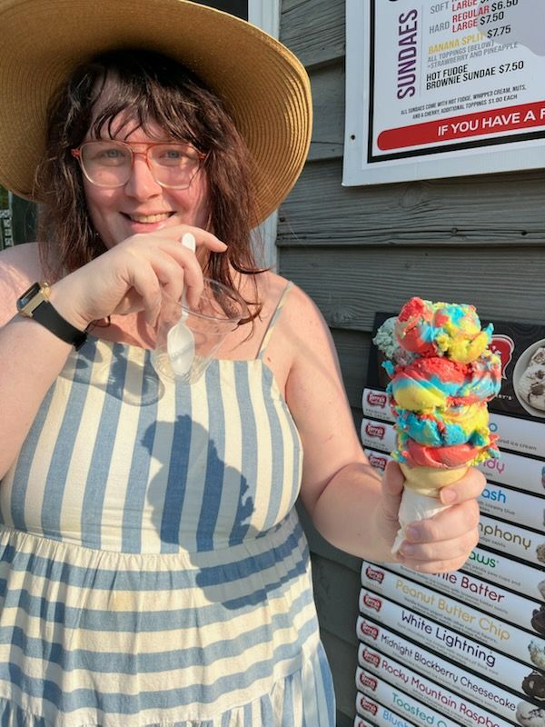 The poster, Jamie Geist, in a white and blue dress and a tan hat, holding a giant ice cream cone