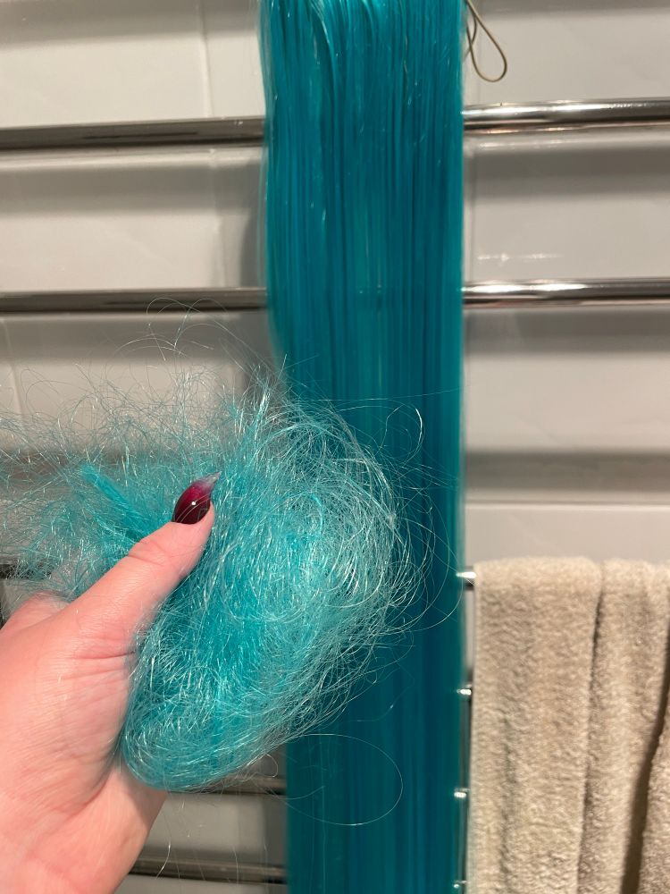 An image of a hung up Miku ponytail wig, with my hand holding the fallout strands from it. 