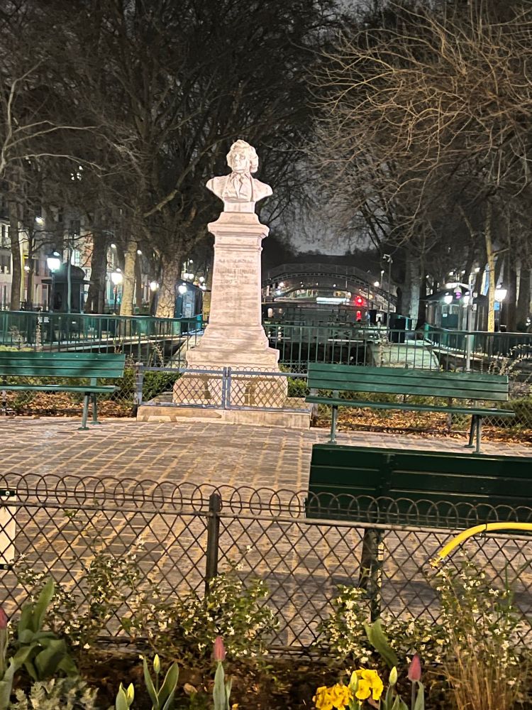 A nighttime picture of the bust of the nineteenth-century actor Frédérick Lemaître in Paris outside in a park with a fence around it.