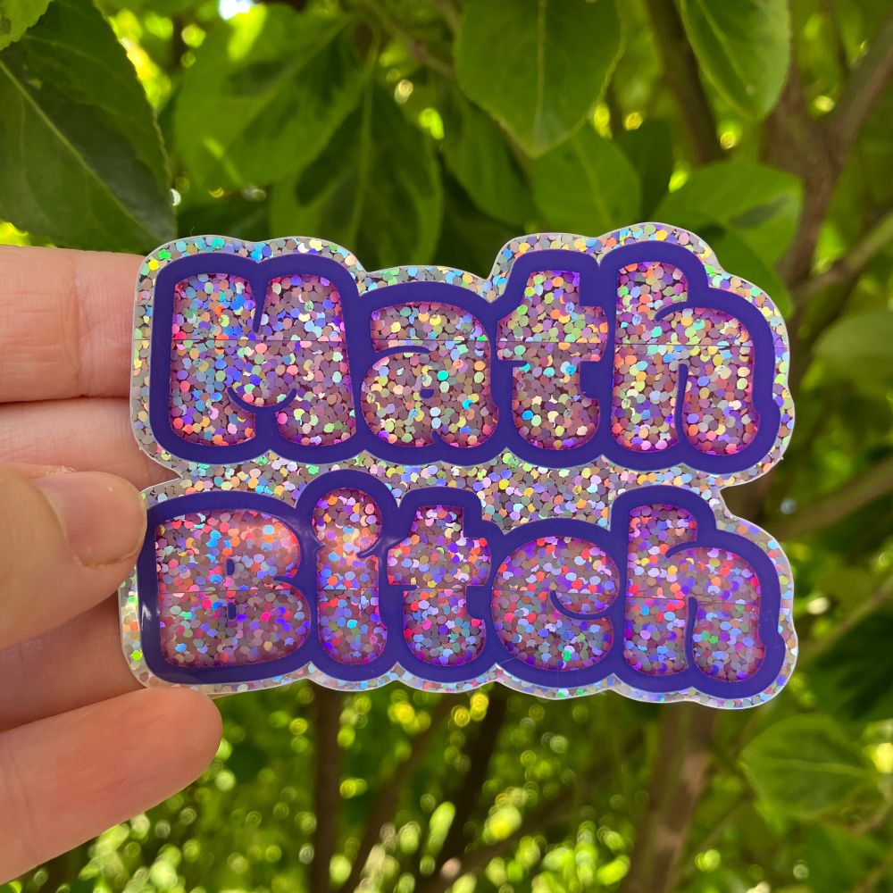 A photograph of a hand holding a sticker in front of some bright green leaves. The sticker features the words "math bitch" in playful, round lettering. The letters are pink with a purple stroke, and the whole thing is glittery and fabulous!