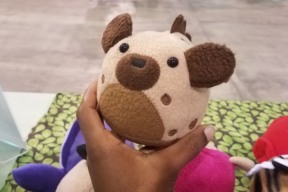 Photo of a recent FuzziPuff hyena, a round, softball-sized simplified plush; held by the artist.