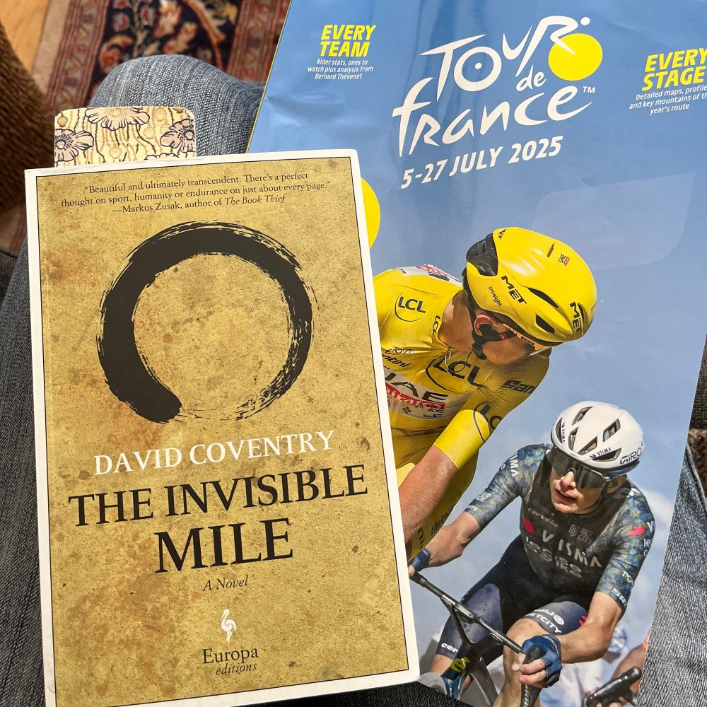 A copy of David Coventry's novel The Invisible Mile with a sand coloured cover with a tire track, sits on a cycling magazine showing Tadej Pogacar looking back at Jonas Vingegaard