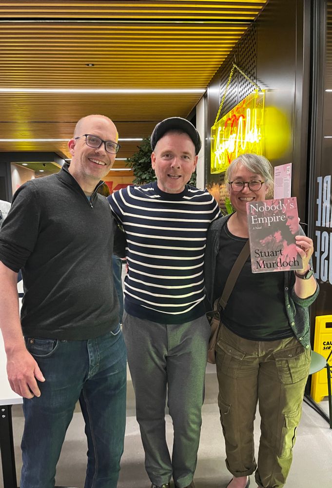 Stuart Murdoch stands in the middle of two fans, one of them - me - holding up a copy of his novel Nobody's Empire. 