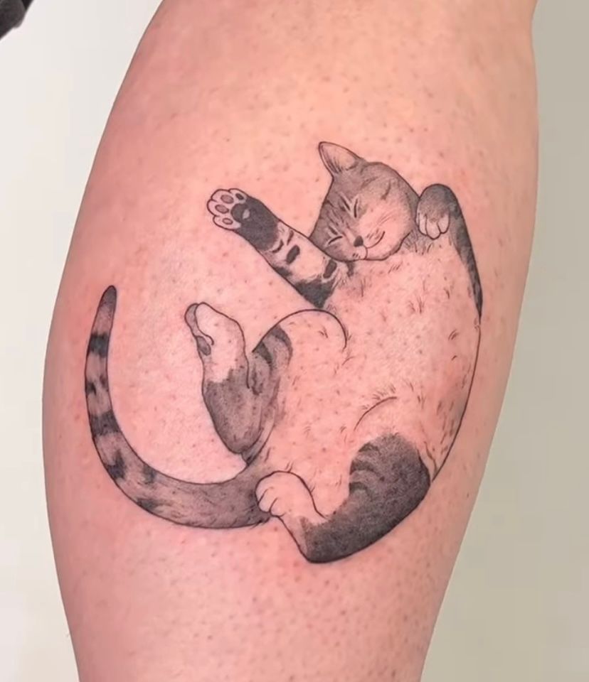 a tattoo of a drawing of a cat laying on its back with belly exposed, smiling