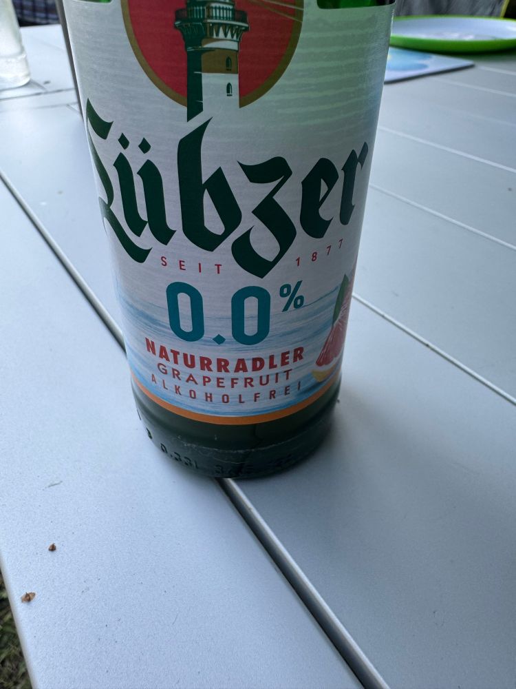 Eine Flasche Lübzer Naturradler Grapefruit 0.0% steht auf einem Alu-Campingtisch