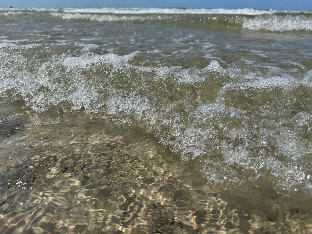 Wellen kräuseln sich, man erahnt blauen Hinmel, die Sonne scheint