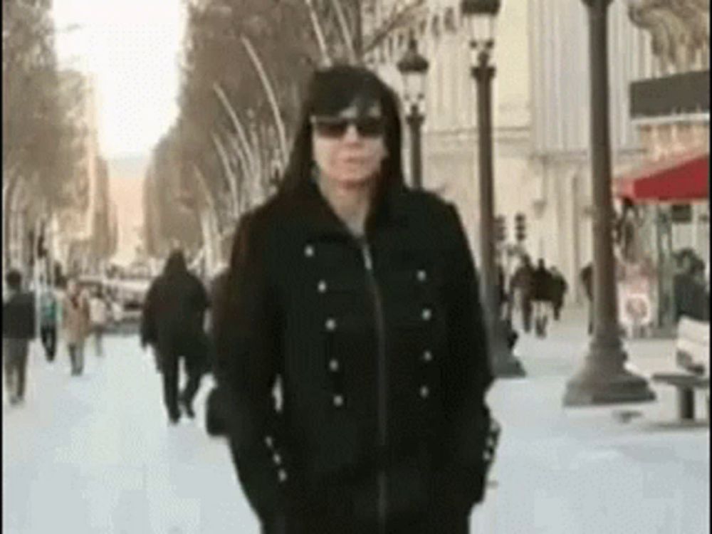 a woman wearing sunglasses and a black jacket is walking down a street .