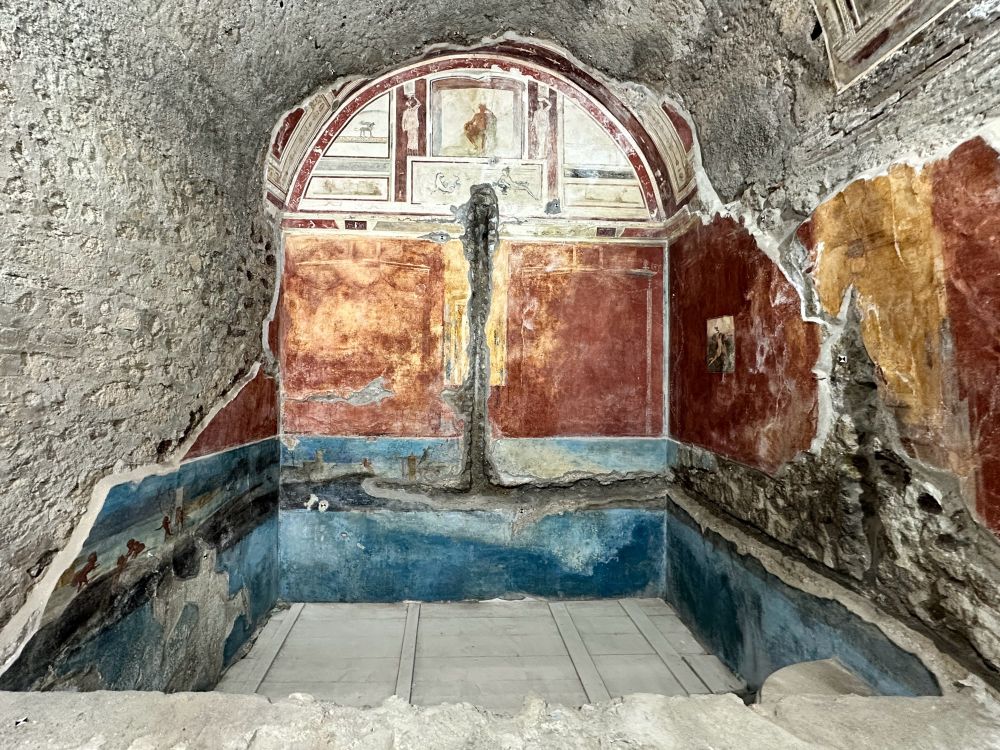 The painted shower pool with a vaulted roof. The arched vault is decorated in white with a representation of the Sarno River. The central painted register are red panels and the lower register is a Nilotic scene. It is thought that a pipe showered water rather than it being stagnant water in a pool.
