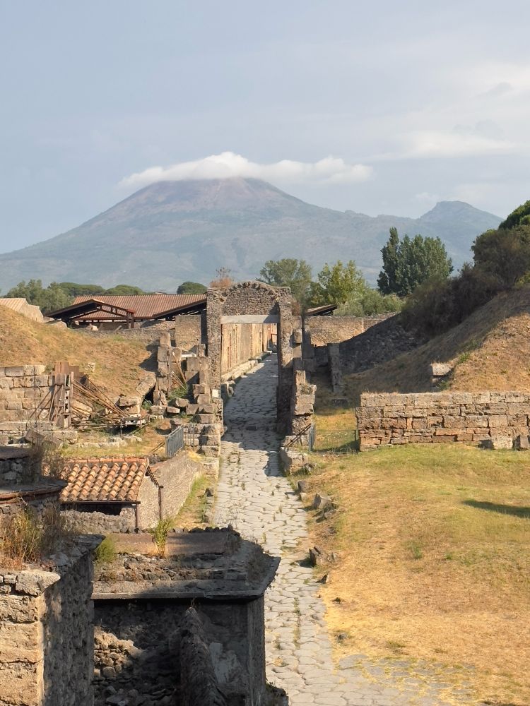 View up the via Nocera through the Nocera gate of Pompeii with Vesuvius in the background with a flat white cloud crowning its peak.