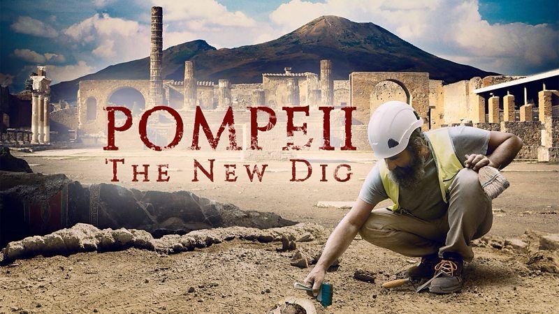 Publicity photo for the programme: in the foreground someone brushes clean a find with pompeii and Vesuvius behind them