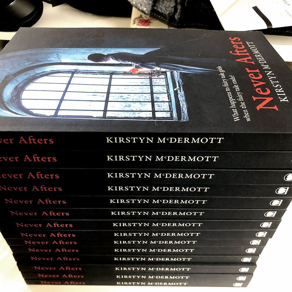 Copies of Kirstyn McDermott's Never Afters stacked fourteen books high, with the cover visible on the top volume. 