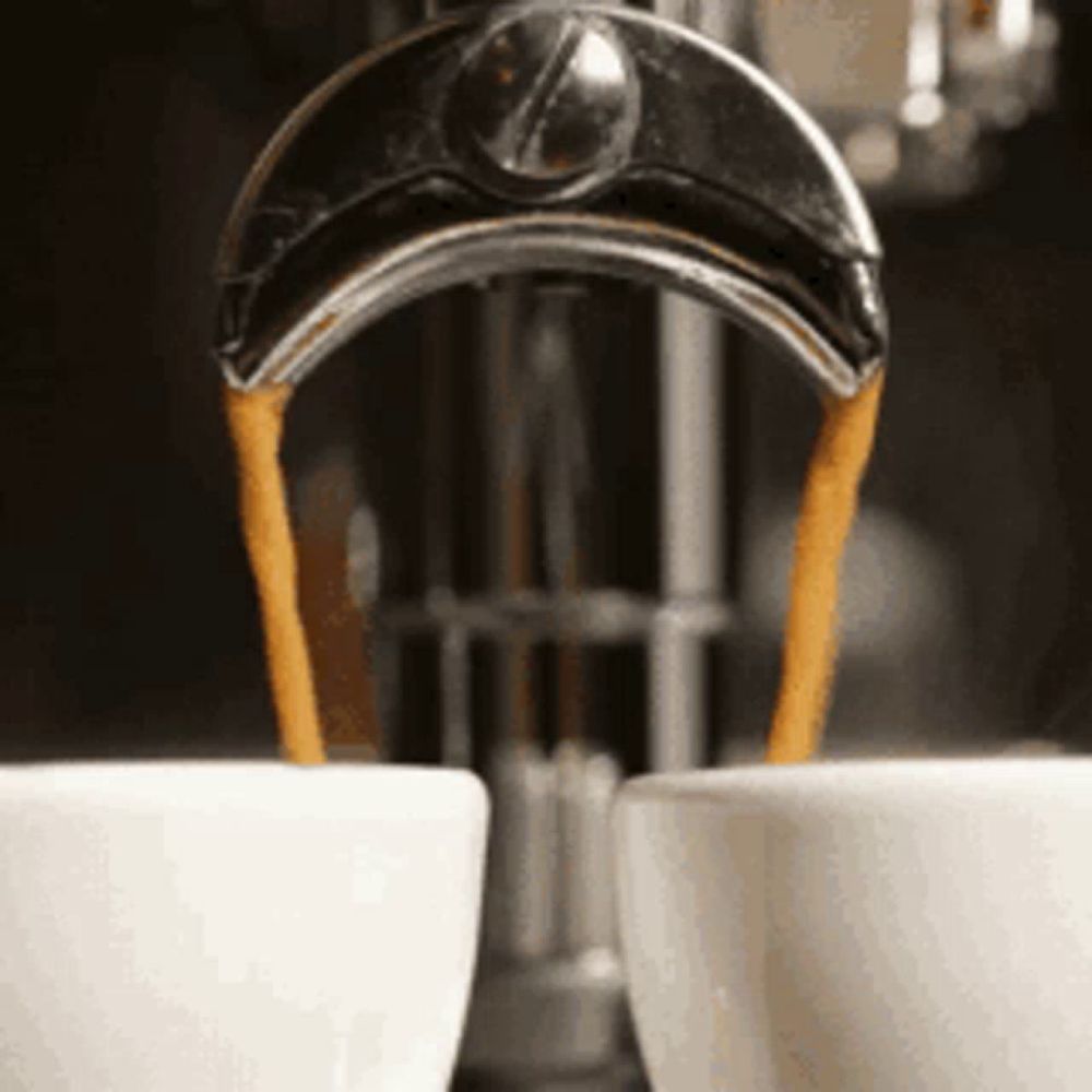 two cups of coffee are being poured into them from a machine