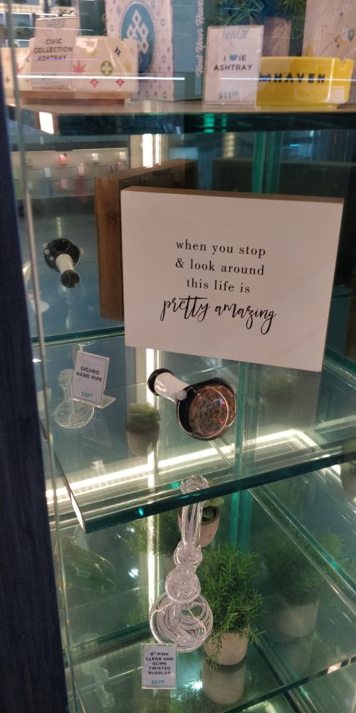 A glass display case full of...glass. Next to a pipe is a home decor thingie that says "when you stop & look around this life is pretty amazing"