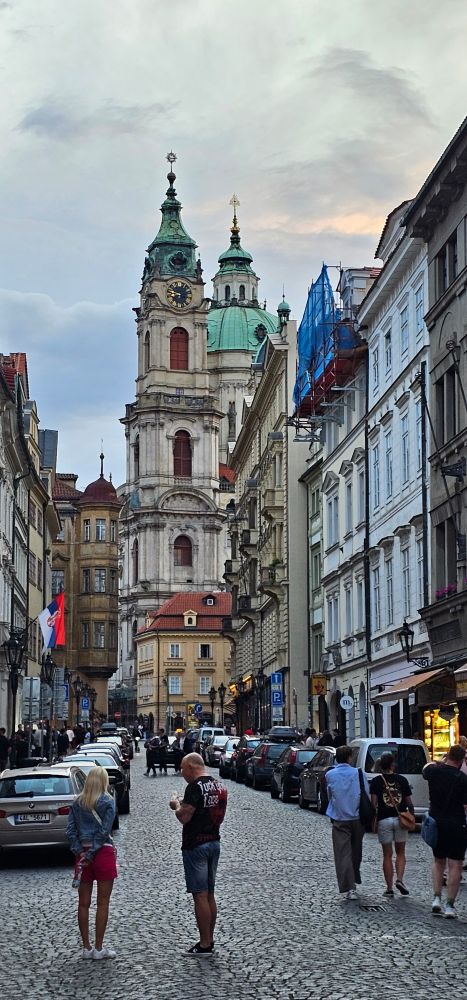 A street in the old town of Prague, leading to an old baroque church with a dome.