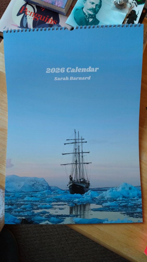 The front cover of a calendar, there is a picture of a wooden tallship surrounded by sea ice and small icebergs. 
