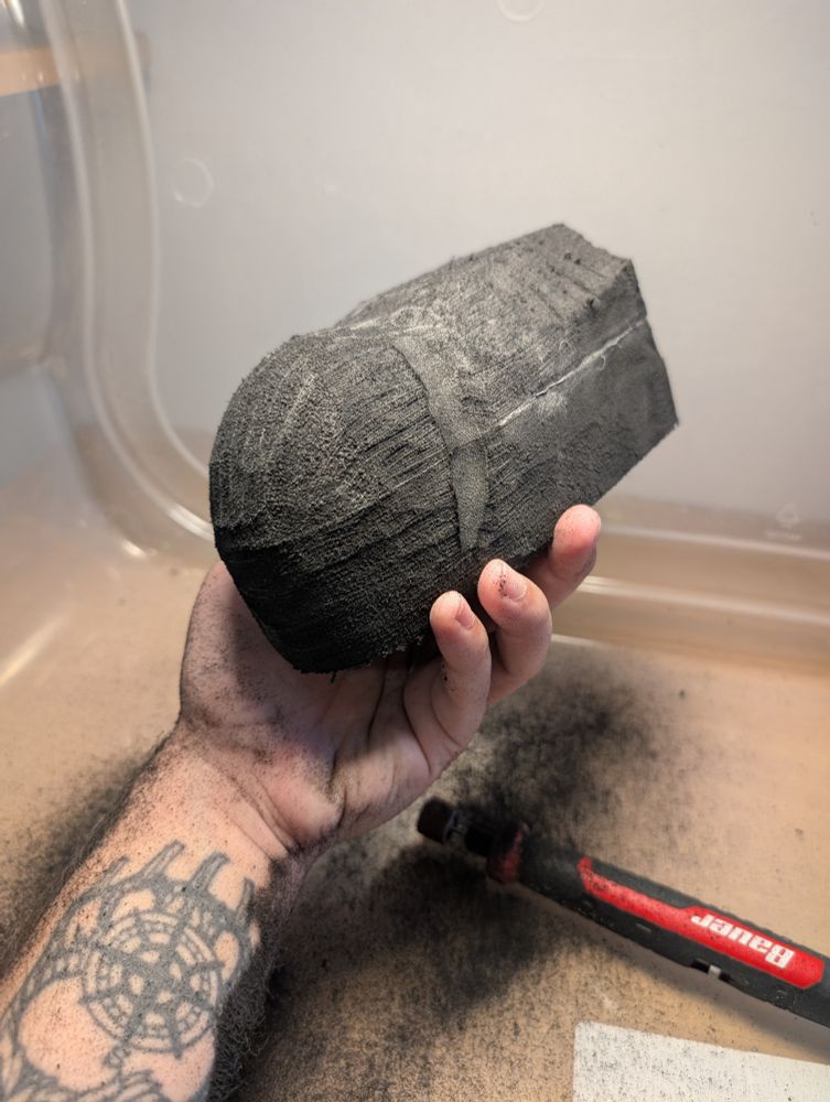 A hand holds a lump of rough foam, a Dremel tool sits close behind it. The beginnings of a dragonish head