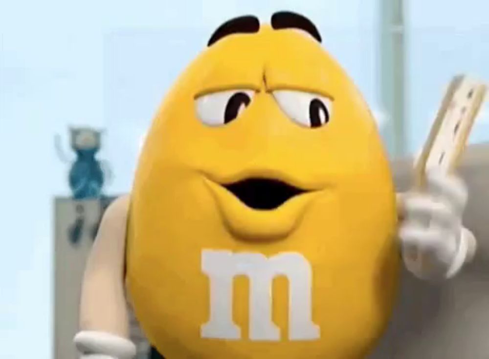 a yellow m & m holding a piece of paper in his hand