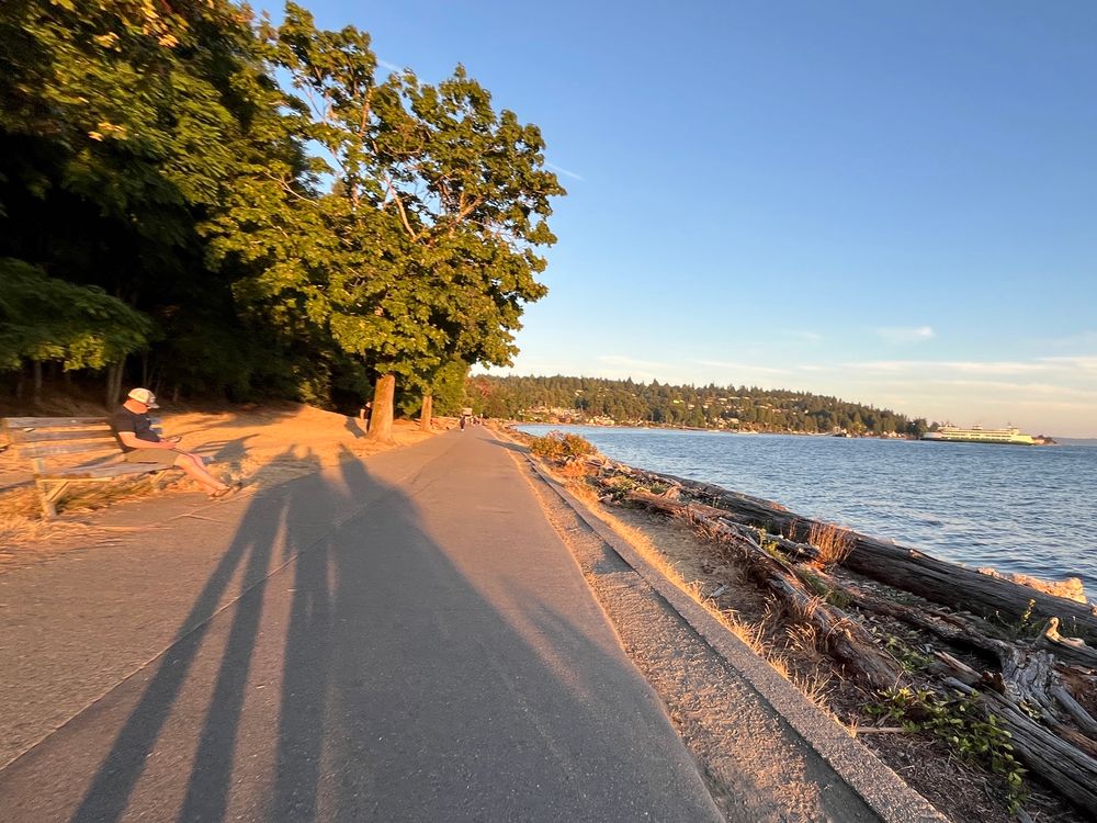 long shadows ahead of three people walking along the shoreline at golden hour in Lincoln Park with a ferry at the dock in the distance