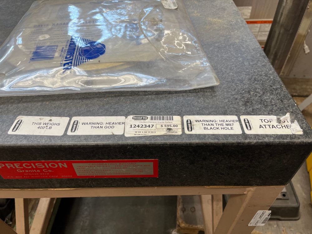a huge precision ground granite slab with stickers on it that say: “THIS WEIGHS 400LB” “WARNING: HEAVIER THAN GOD” “WARNING: HEAVIER THAN THE M87 BLACK HOLE”