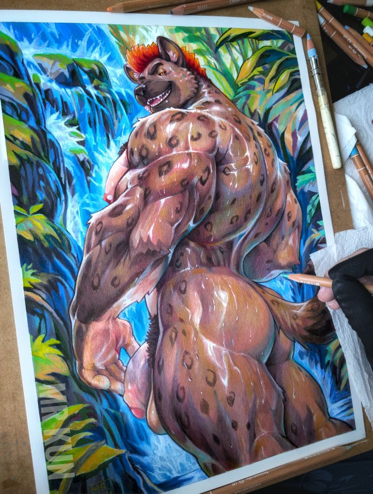 A traditional illustration in progress, showing a muscular anthropomorphic hyena with brown spotted fur, standing confidently in front of a lush jungle and  waterfall. He has fiery red-orange hair and he is turning his head back with a smug smile. His large, defined muscles and round butt are prominently featured, with the artist's gloved hand visible holding a colored pencil, adding detail to the fur. Art supplies, including pencils, tissues and a blending tool, are scattered around the image.