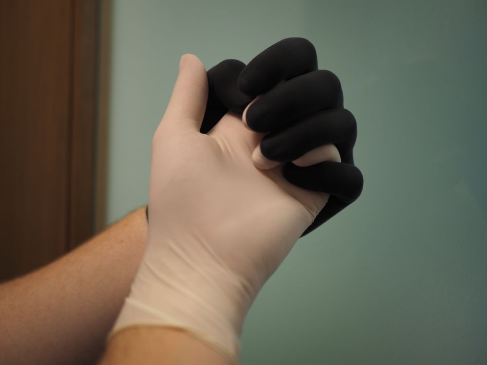 A close up of two people holding hands. One hand is wearing a black glove and the other is wearing a white glove