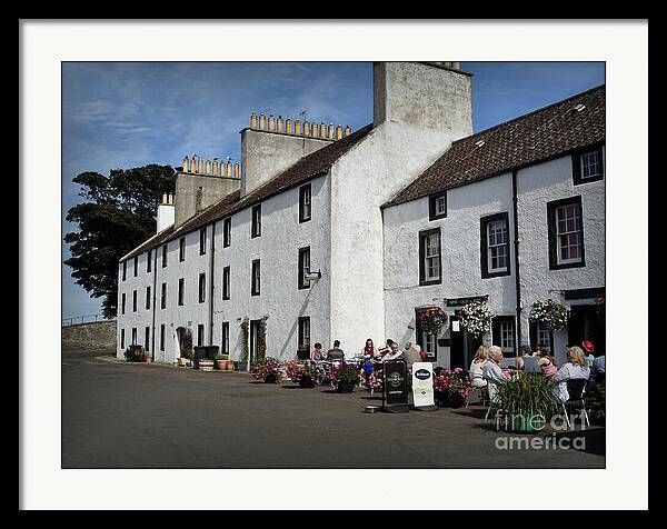 Cramond is a village and suburb in the north-west of Edinburgh, Scotland. It stands at the mouth of the River Almond, where it enters the Firth of Forth.
The area has a long history, with evidence of Mesolithic, Bronze Age and Roman activity.
The older houses along the wharf are typical of traditional south-east Scottish vernacular architecture, constructed in stone with harling white lime render finish, facing stone windows and door surrounds.
The image is an idyllic Summer scene with blue skies, opposite the wharf and shows people dining outside the village inn. The area is decorated with floral hanging baskets and planters. The houses and Inn are white washed with black painted doors and window surrounds.