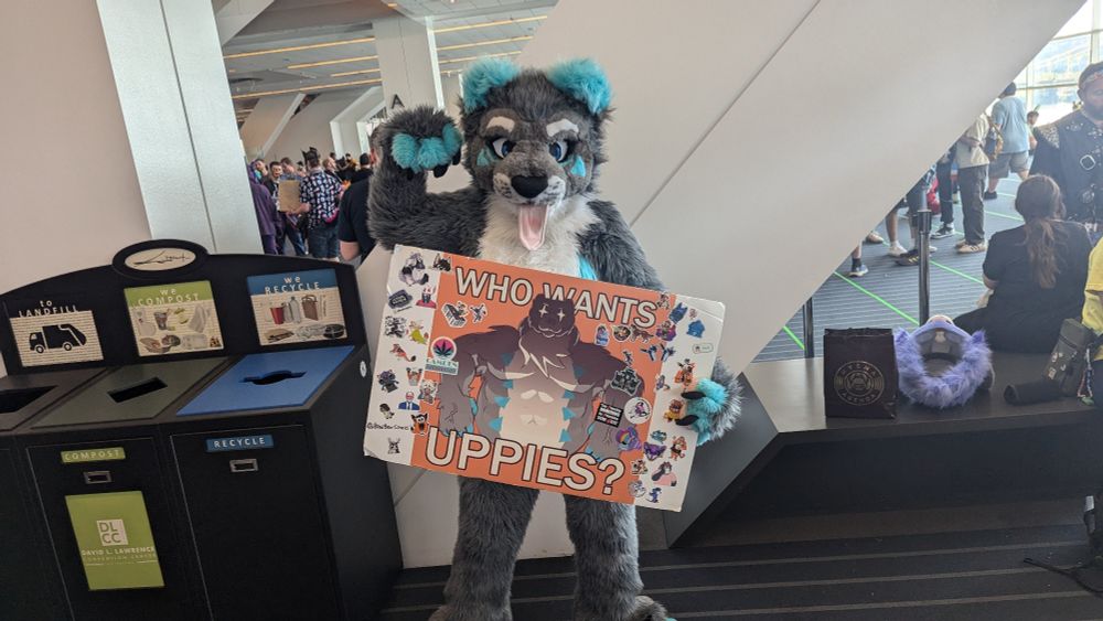 It's a person I'm a canine fursuit, they are pointing to a sign that says "Who wants uppies" with a very menacing drawing of their fursona in the background. 