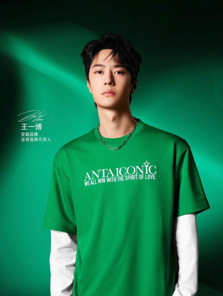 Wang Yibo in a green tee shirt worn over a white long sleeved tee shirt.