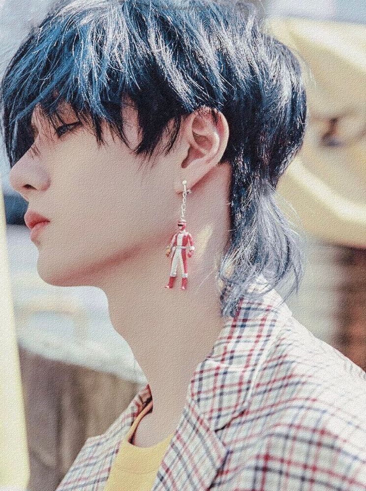 Head and shoulders photo of Wang Yibo in profile, wearing a check blazer over a yellow tee, sporting a blue highlighted mullet and wearing a dangly earring in the form of an ultraman figurine.