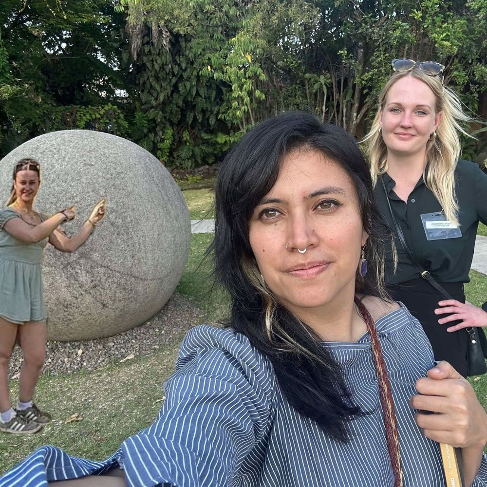 Two women pose with an ancient large stone sphere, with another woman photoshopped in