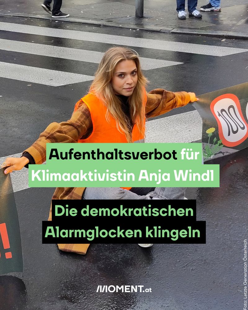 Eine Klimaaktivistin in orangefarbener Warnweste sitzt mit ausgebreiteten Armen auf einer regennassen Straße bei einer Protestaktion. Der Text darüber lautet: „Aufenthaltsverbot für Klimaaktivistin Anja Windl. Die demokratischen Alarmglocken klingeln.“