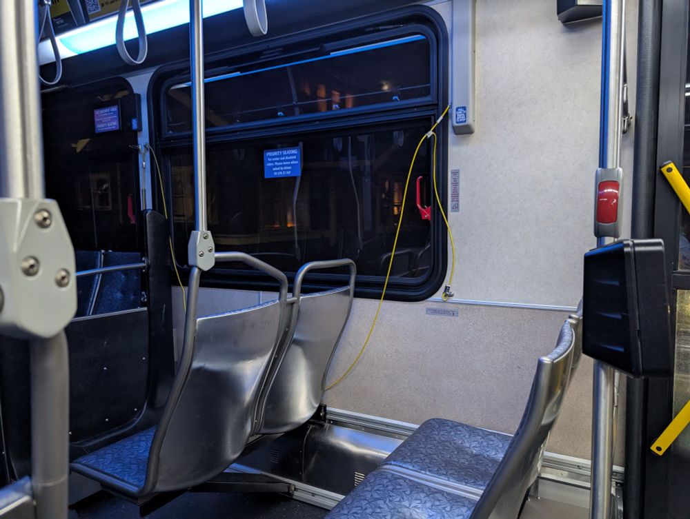 A photograph of an empty bus at night. The yellow pull string has broken and is dangling in a long loop down near the floor.