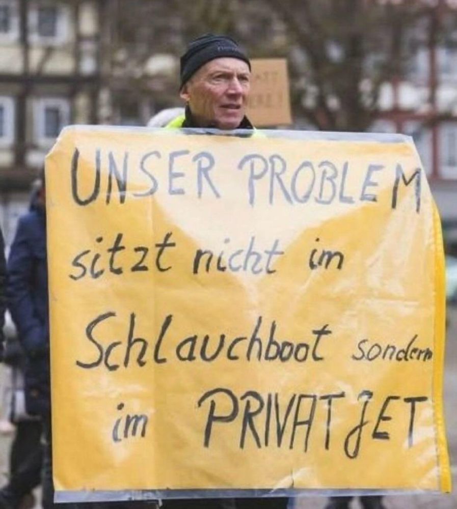 Mann mit Schild, unser Problem ist nicht im Schlauchboot sondern im Privatjet