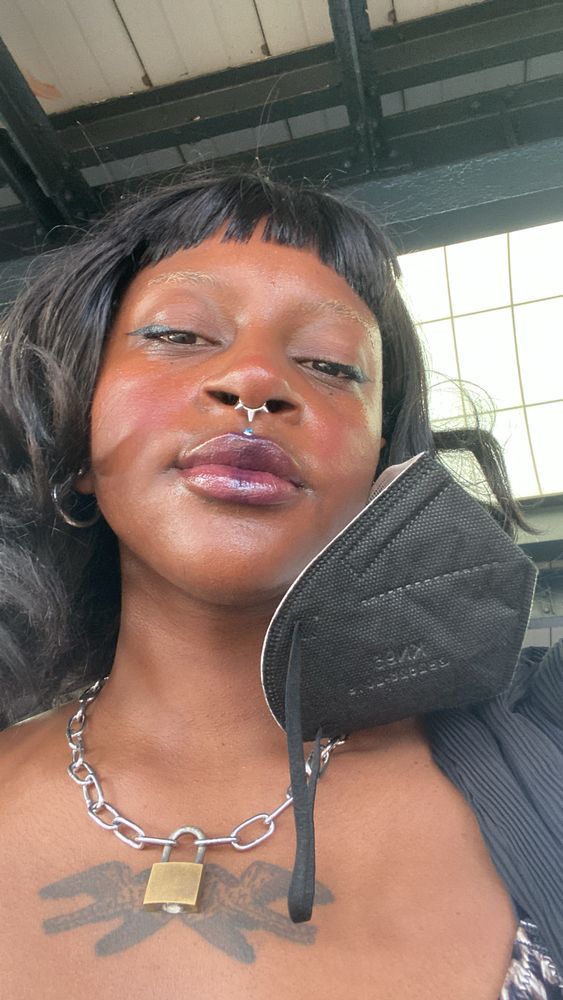 a selfie of Mistrix Salem with their mask off but hanging from one ear, showing their makeup. They wear a plum lip combo.