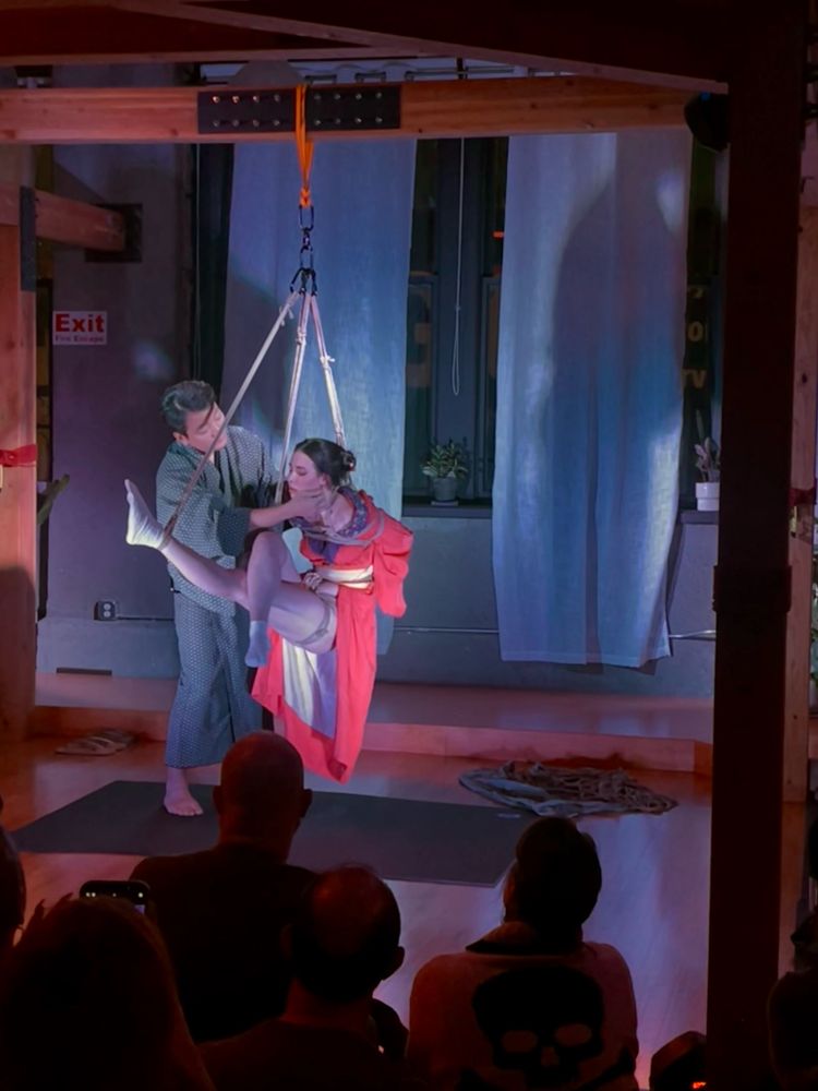 Kinoko and Casey during their Shibari performance. He is gently moving a piece of hair behind her ear. 