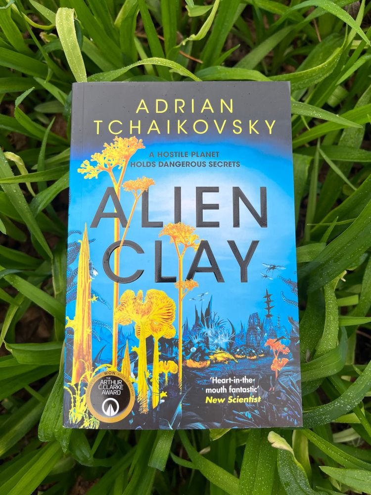 The cover of Alien Clay by Adrian Tchaikovsky featuring vivid yellow fungus things. 