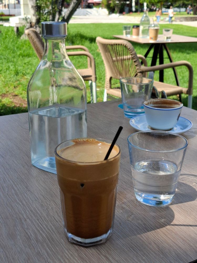 Café frappé, Wasser in Gläsern und einer Flasche und eine Tasse Kaffee auf einem Tisch