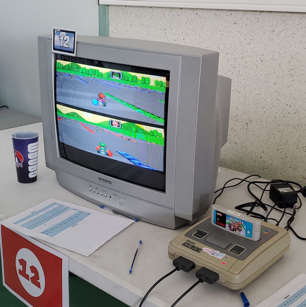 Une télé cathodique avec le Battle Mode de Super Mario Kart affiché.
Une SNES est branchée à côté 