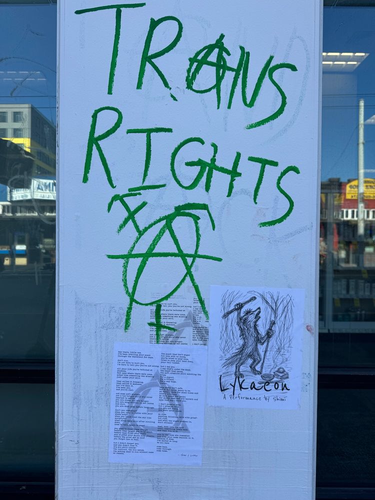 Image 1 (Graffiti wall with flyers): A poster-covered wall in an urban area features vivid green graffiti that reads “TRANS RIGHTS” in large, capital letters. The letter “A” in “TRANS” is stylized as the anarchist symbol—a circled A. Below the text are additional anarchist symbols, drawn roughly in the same green. Affixed to the wall are two printed flyers: one is a typed poem — a performance script; the other is a black-and-white sketch-style flyer for “Lykaeon – A Performance by Shimi,” depicting a humanoid wolf holding a flute in one paw and a staff in the other, howling or shouting upward beneath a tree-like background. 