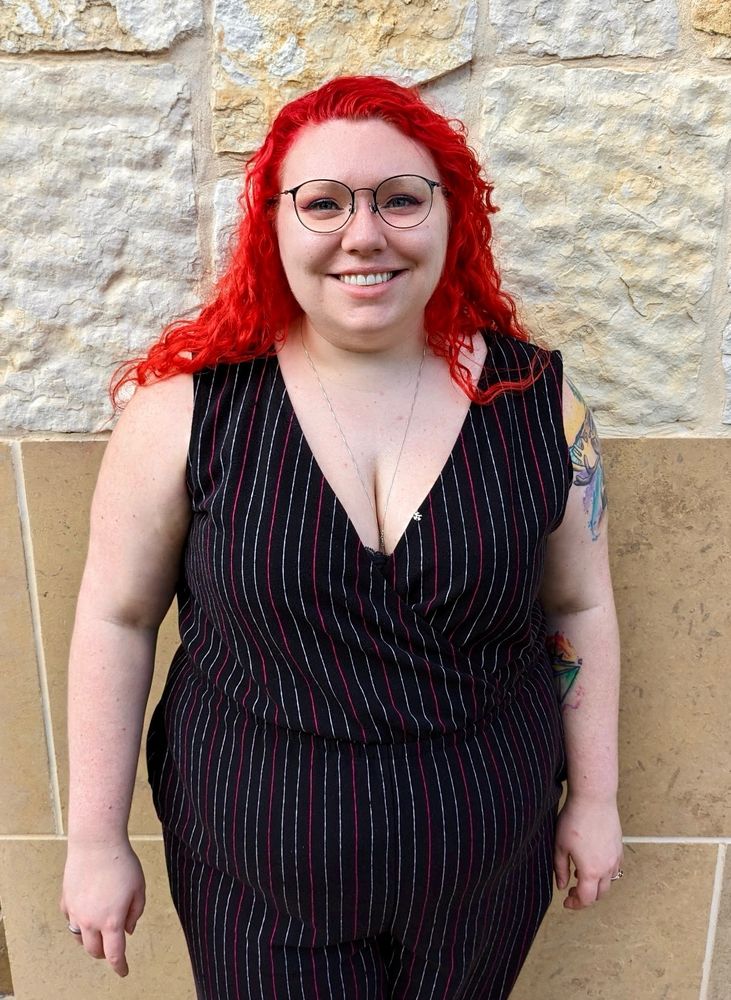 Kylie Sullivan standing and smiling with bright red hair and a striped outfit.