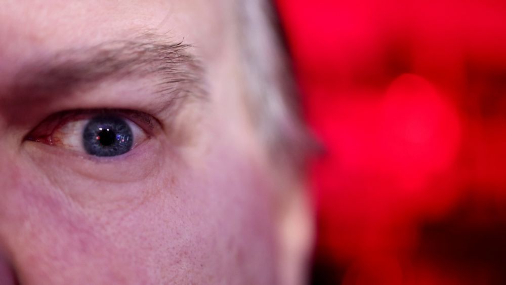 Extreme closeup of my face, only one eye and eyebrow visible, the background is an artistic blurrof reds and blacks