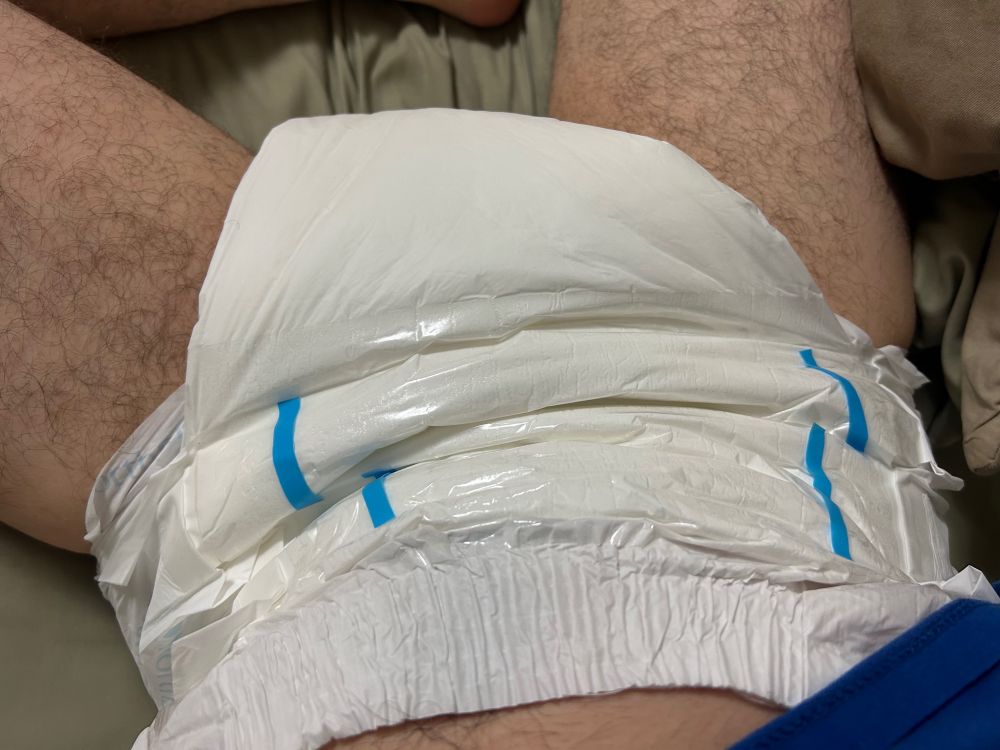 Slim guy laying on a bed in a white Northshore Megamax diaper, size small.