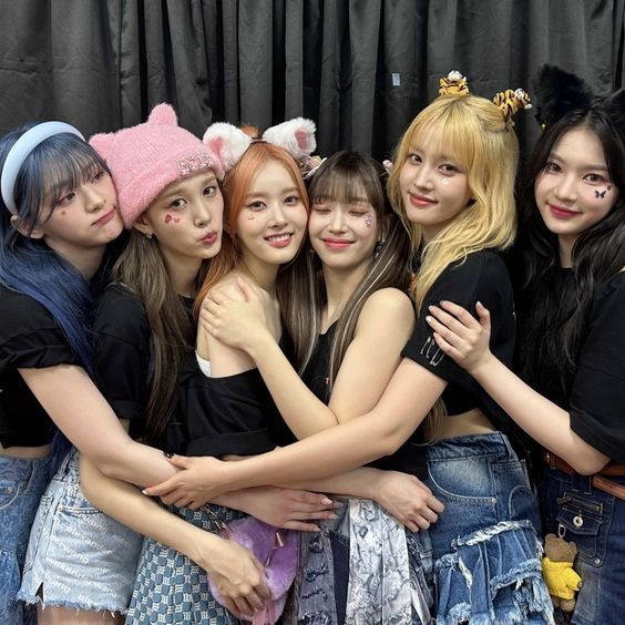 Members of STAYC: Seeun, J, Sieun, Sumin, Yoon, and Isa hug and smile. They are all wearing black tshirts and various denim shorts and skirts following a performance