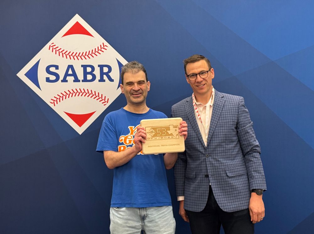 Mark Simon holds his SABR 53 trivia plaque with emcee Dan Massey in front of a blue SABR logo backdrop.