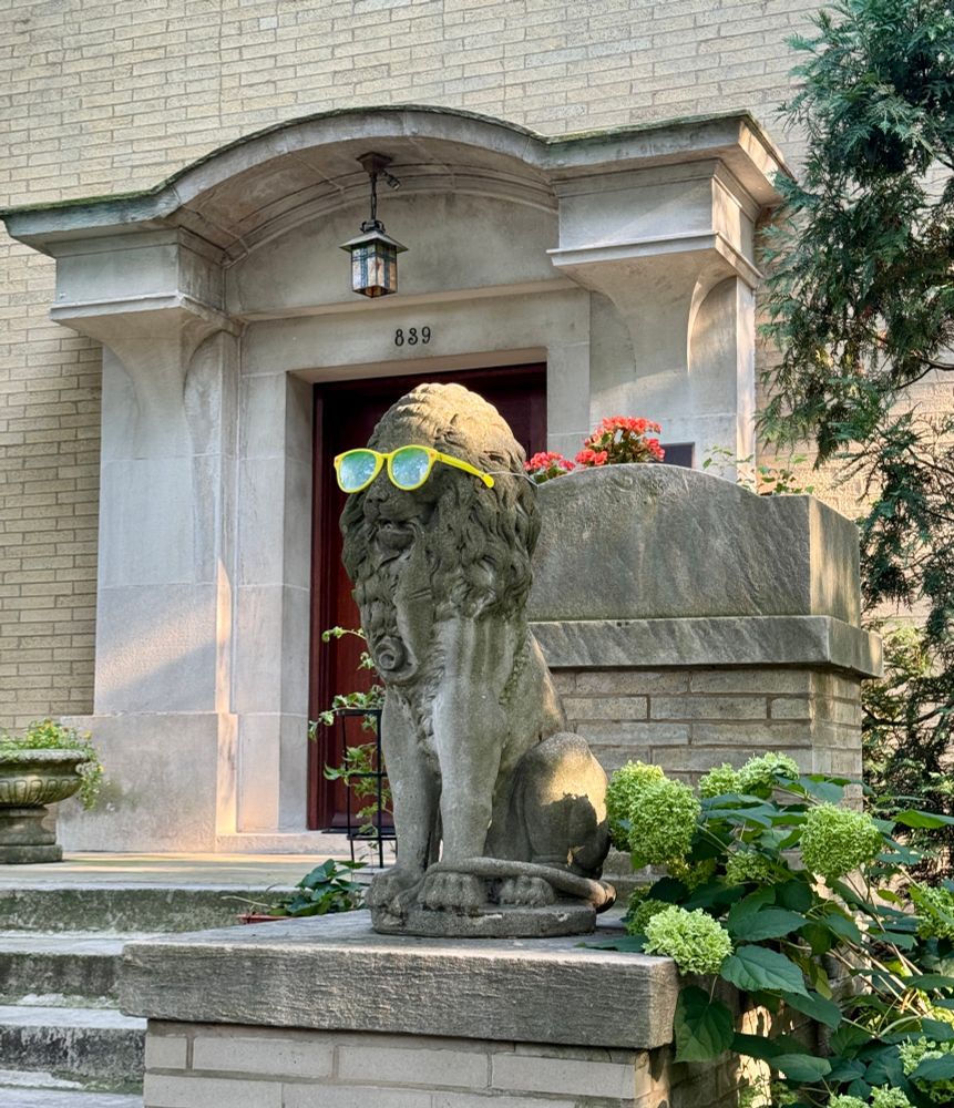 Closeup of a lion statue wearing large yellow sunglasses in front of a Prairie-style house designed by George Maher at 839 W. Hutchinson St. in Chicago.